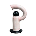 Decorative vase shaped like a letter 'F' with pink flowers on a wooden stool against a white wall.