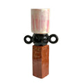 Decorative vase shaped like a letter 'F' with pink flowers on a wooden stool against a white wall.