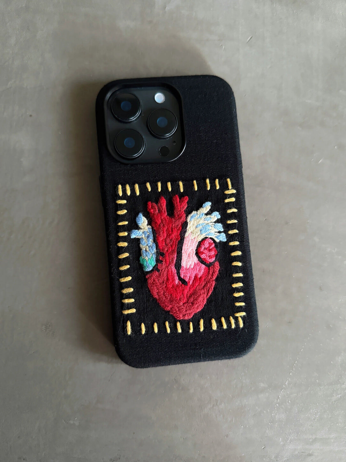 Embossed heart embroidery on TRLab Shop phone case, showing detailed stitched red heart design on a protective cover.